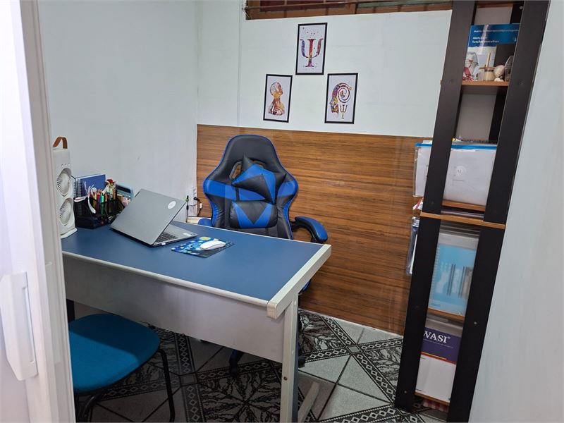 Sala de atendimento com mesa de trabalho, cadeira e estante de materiais
