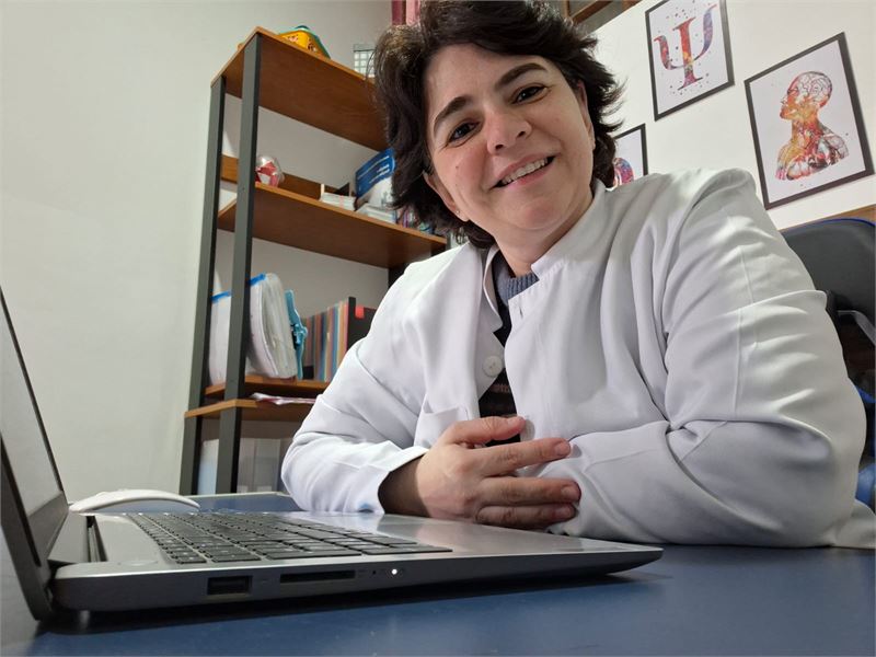 Ana Luiza no consultório, de jaleco, à mesa de atendimento
